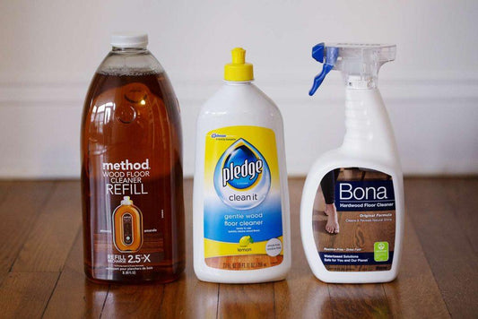 Three hardwood floor cleaner bottles on polished wood floor, including Method, Pledge, Bona.