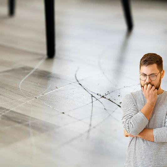 Worried man looking at scratched hardwood floor with chair legs in background